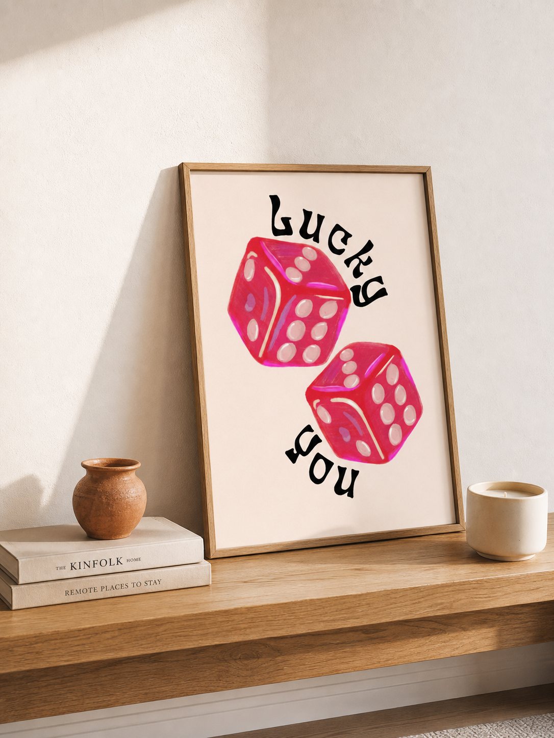 Lucky dice art print with pink-red dice and black typography displayed on a bright warm white wall above an oak console, styled with a ceramic vase for playful modern decor.